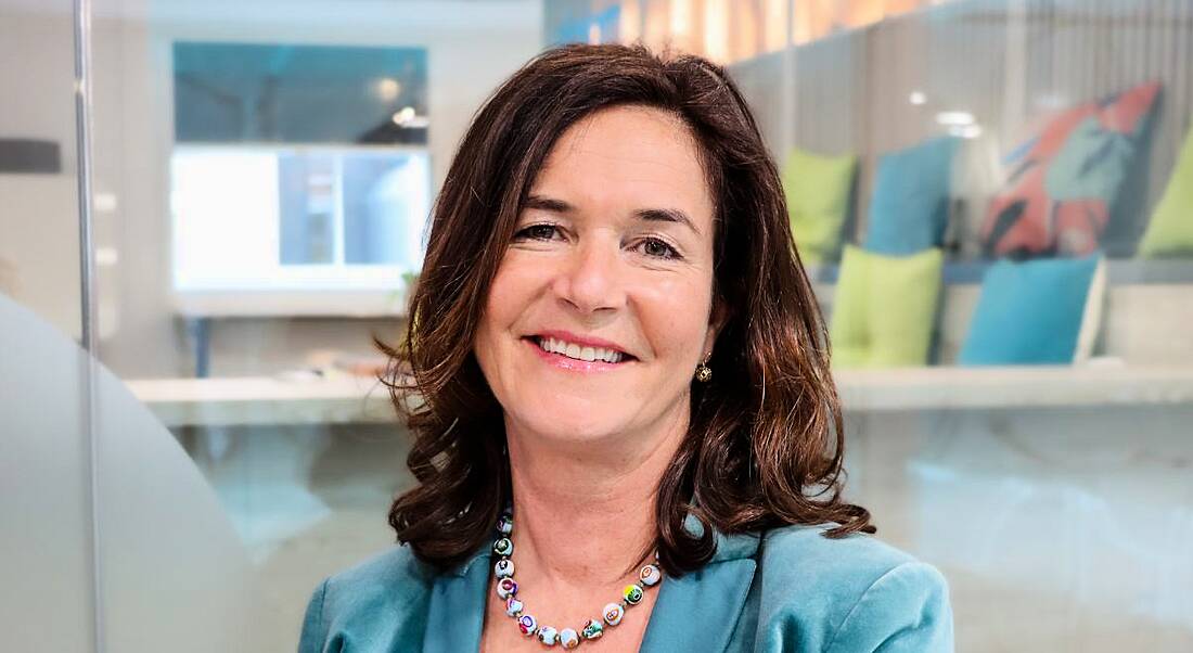 A woman wearing a blue blazer smiles at the camera in a brightly lit room. She is Jane Dawson-Howe of Slalom.