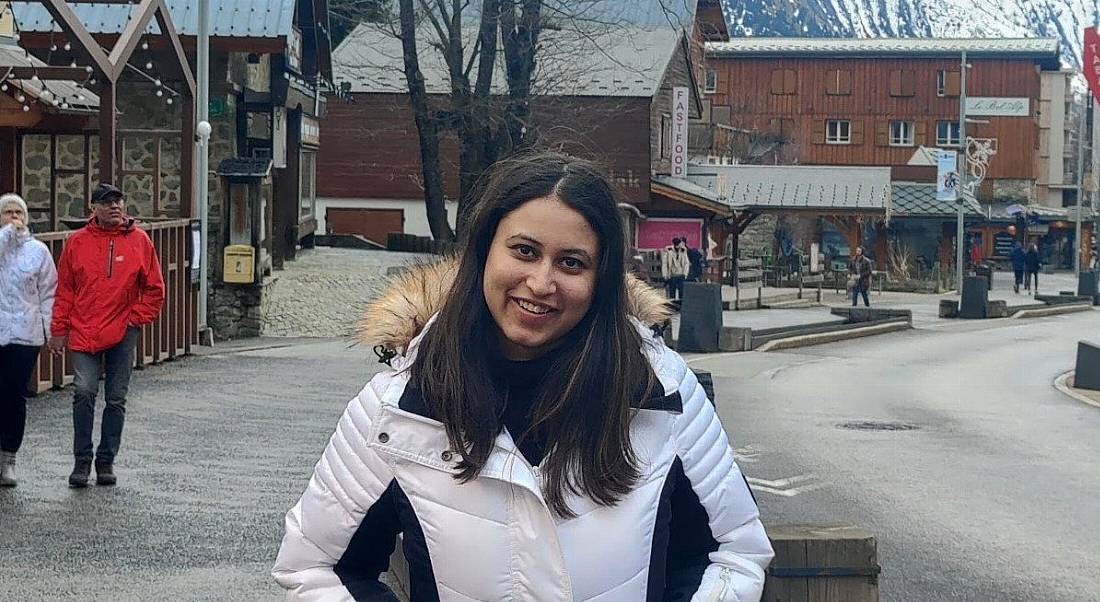 A woman wearing a white winter jacket smiles at the camera on a town street.