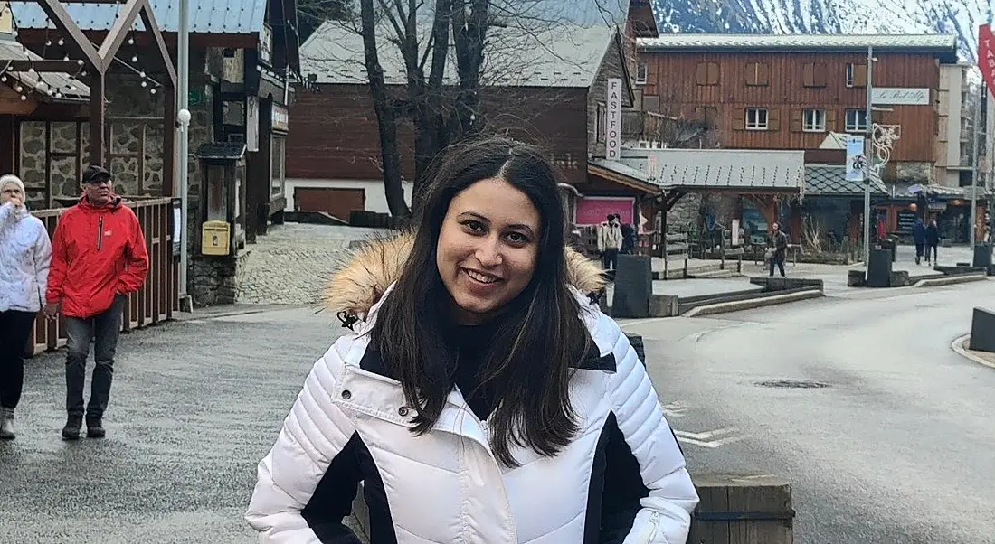 A woman wearing a white winter jacket smiles at the camera on a town street.