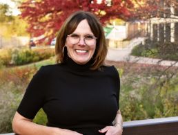 MD of GlobalLogic Carmel Owens poses in a green coat in front of a building.