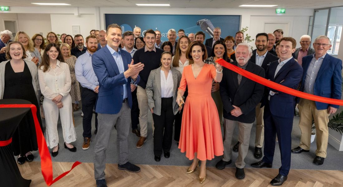 A crowd of men and women in an office as a red ribbon is cut in front of them. The opening of the new Loci Orthopaedics office.