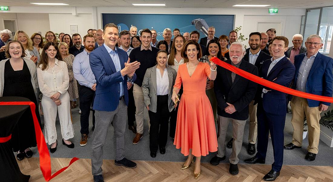 A crowd of men and women in an office as a red ribbon is cut in front of them. The opening of the new Loci Orthopaedics office.