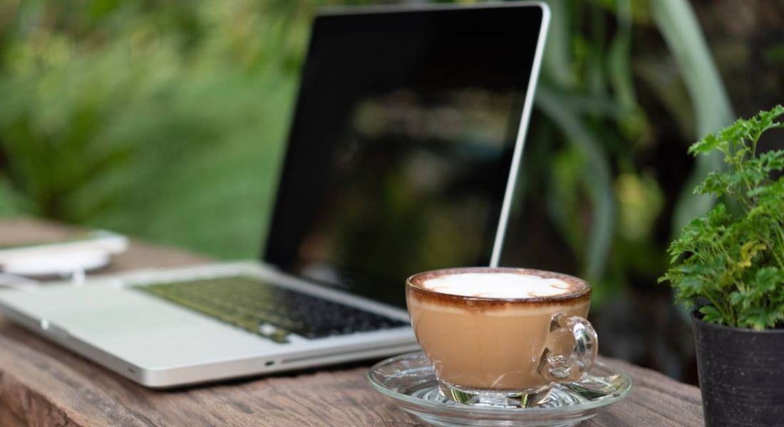 A coffee mug sits on a wooden desk next to a laptop, representing the peacefulness of outdoor working environments.