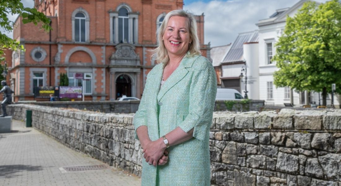 MD of GlobalLogic Carmel Owens poses in a green coat in front of a building.