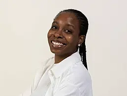 A brunette woman smiling at the camera wearing a black flowery blazer. The BMS office is blurred out behind her.