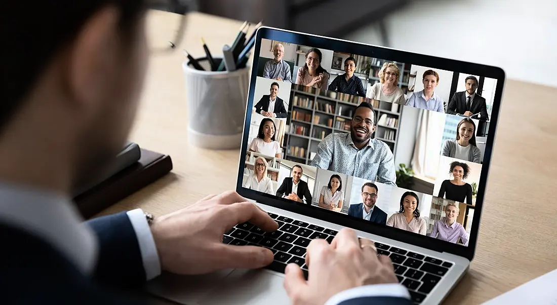 A worker looks at his screen as his diverse co-workers engage with him and each other from their remote-based offices.