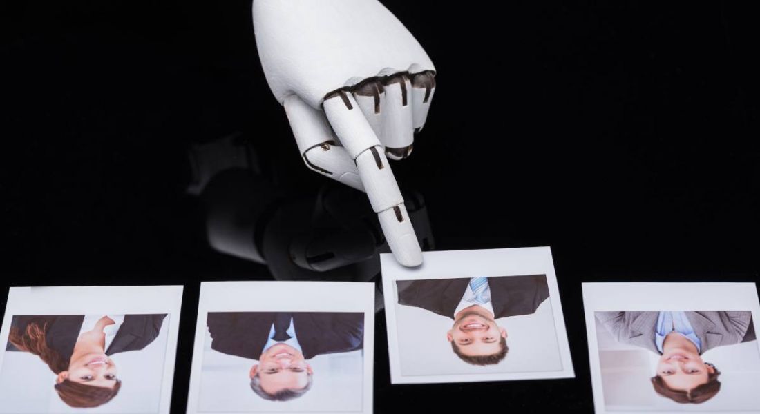 A robotic arm is picking out a male image from a line of job candidates, representing AI in the job application and recruitment process.