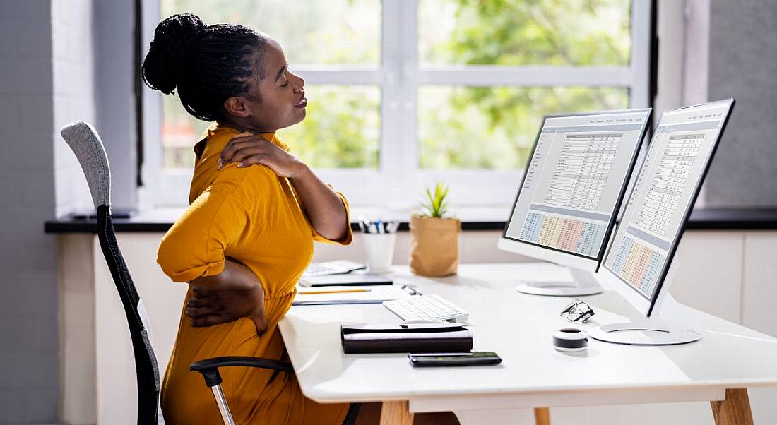 A woman in a yellow outfit sits at a desk trying to get comfortable, representing the importance of an ergonomic office design.