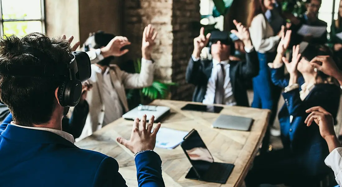 A work group are crowded around a table using VR in the workspace.