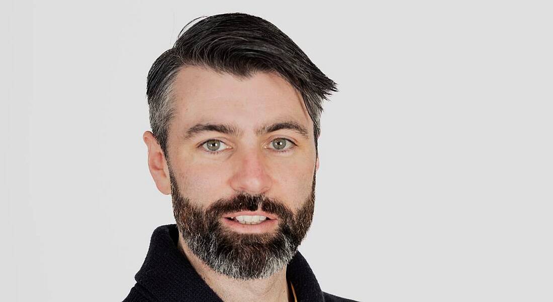 A headshot of a man smiling in front of a white background. He is Eoghan Powell of Work IQ.