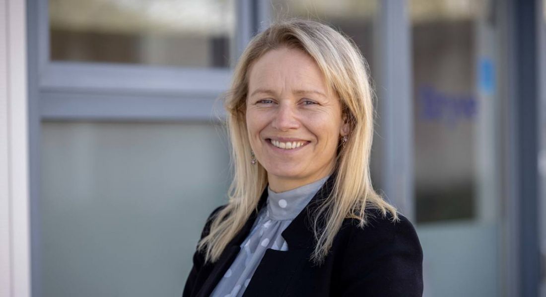 An image of a blonde woman smiling in front of a building. She is Gillian Moody.