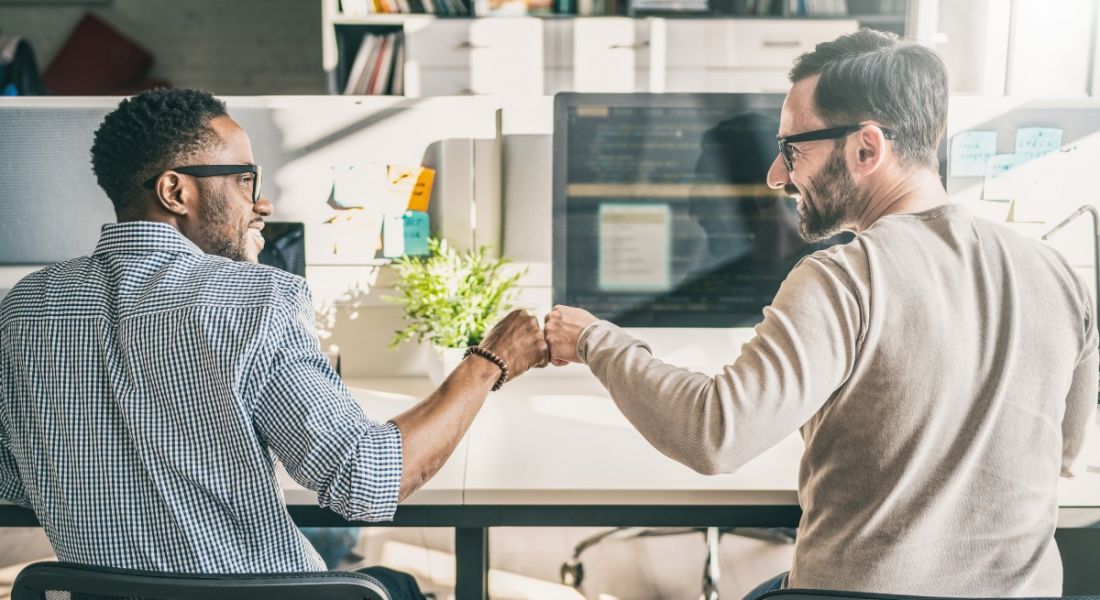 Two men fist-bump each other in the office, signalling a work-based friendship.