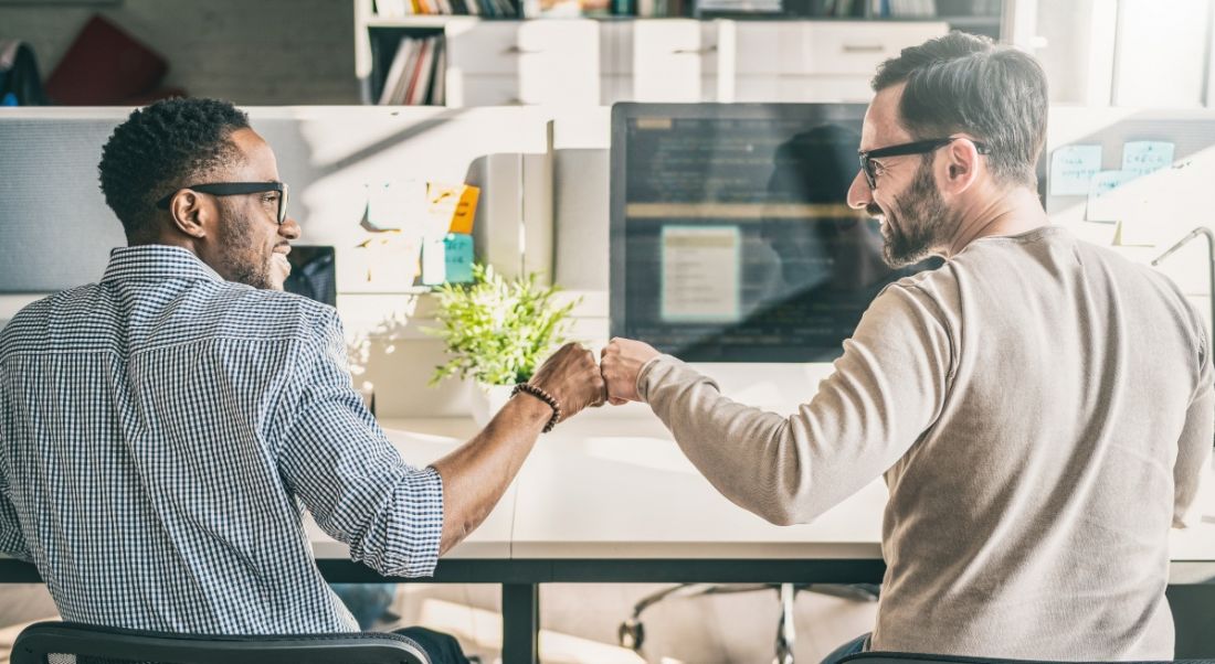 Two men fist-bump each other in the office, signalling a work-based friendship.