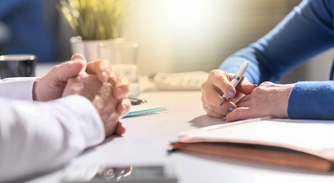 Two people sit at a table, with their hands clasped together in a position indicating a workplace negotiation.