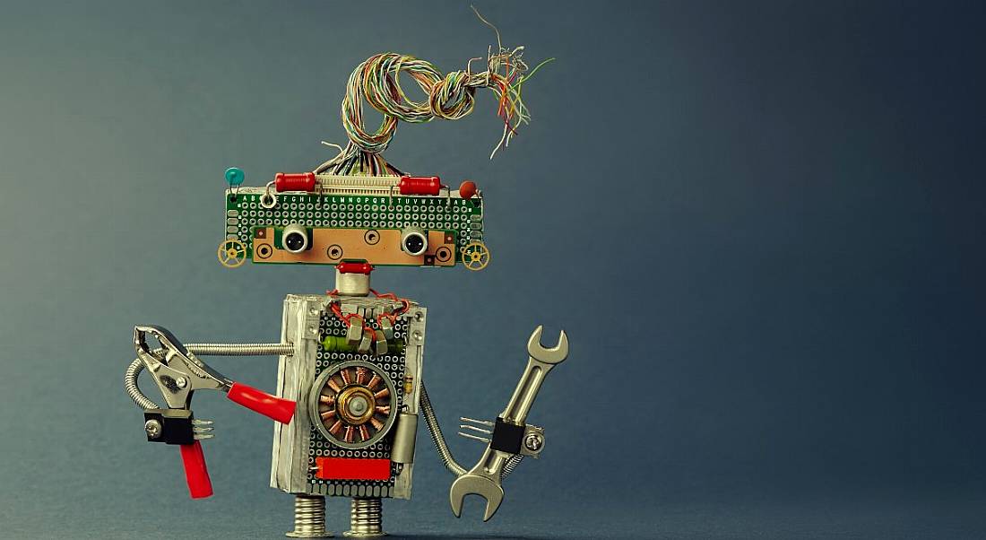 A metal toy robot made up of various electrical components. It is holding a wrench and pliers.