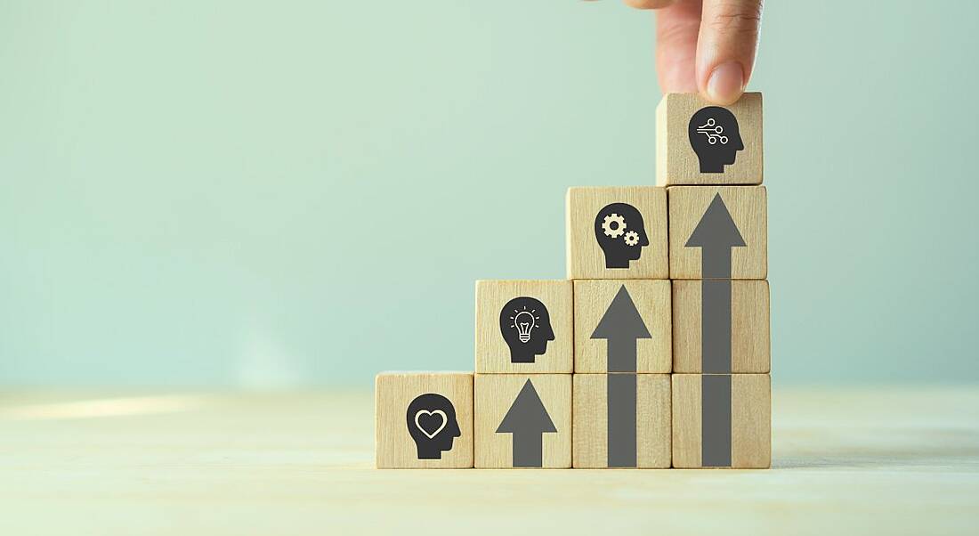 Wooden blocks stacked in an ascending stairs fashion. Each one top one has a head with skills symbols in them, while the stacked ones beneath make arrows.