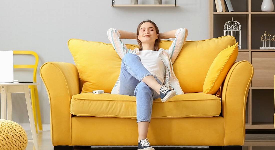 A woman relaxes on a bright yellow couch in the comfort of her home.