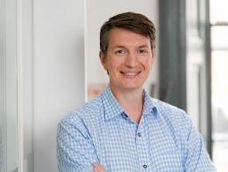 A woman in a green blazer leans on a grey wall in front of an out-of-focus window. She is the MD of Optum UK and Ireland.