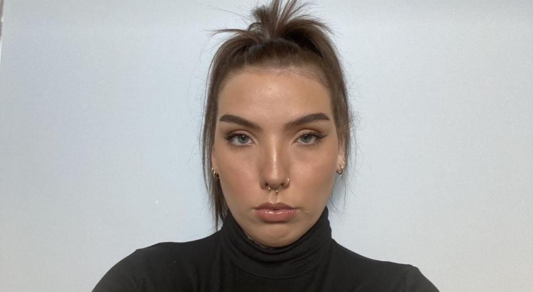 A woman wearing a dark turtleneck with her hair tied up looks into the camera in front of a grey wall. She is Mallaidh Downes, a cloud engineering consultant at Deloitte.