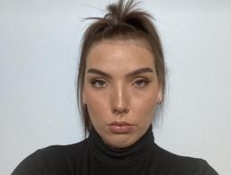 A woman wearing a white shirt smiles at the camera in front of an off-white background.