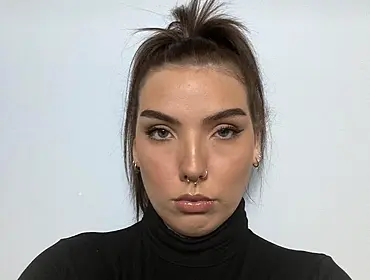 A woman wearing a dark turtleneck with her hair tied up looks into the camera in front of a grey wall. She is Mallaidh Downes, a cloud engineering consultant at Deloitte.