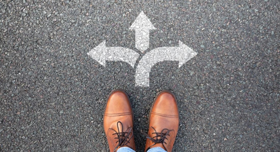 A pair of brown shoes stand at a three-pointed arrow, trying to decide the right path.