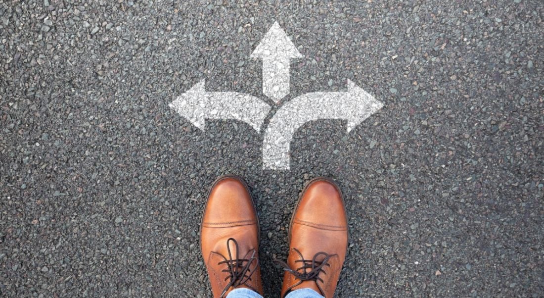 A pair of brown shoes stand at a three-pointed arrow, trying to decide the right path.