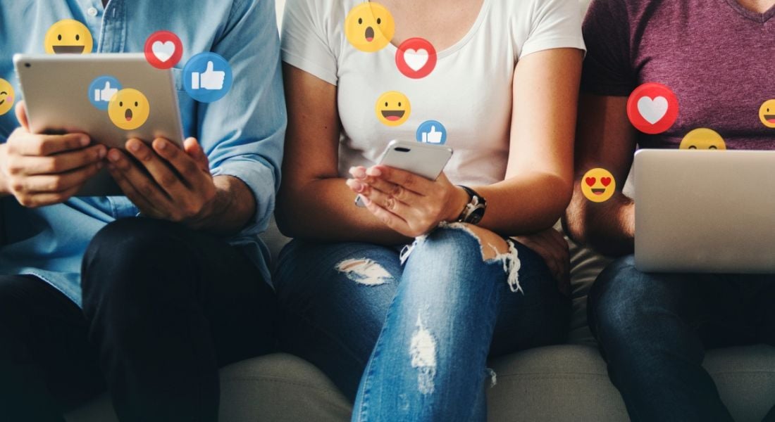 Three employees sit side by side working on their different digital devices and engaging with social media.