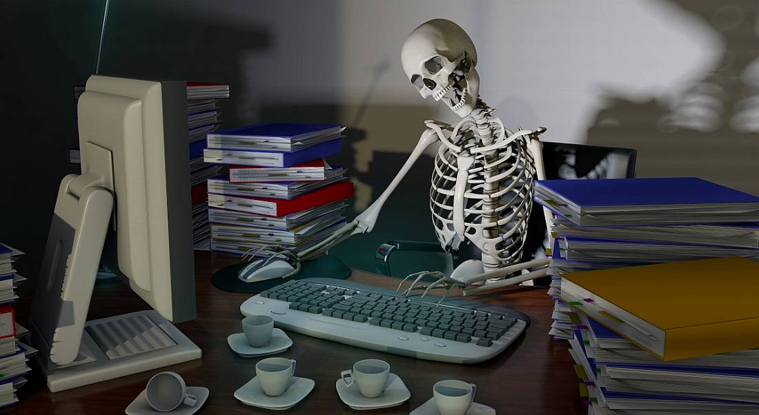 A skeleton works at a desk, representing the danger of overworking to physical, emotional and mental health.