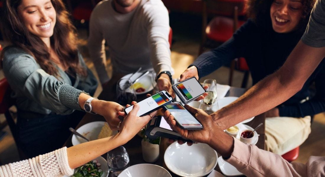 Multiple people holding smartphones above a table, with digital Bunq cards on the smartphone screens.