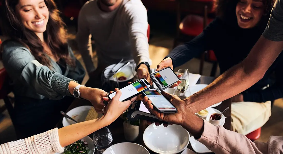 Multiple people holding smartphones above a table, with digital Bunq cards on the smartphone screens.