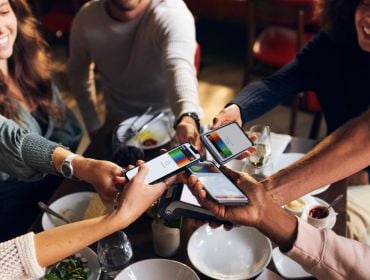 Multiple people holding smartphones above a table, with digital Bunq cards on the smartphone screens.