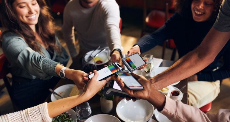 Multiple people holding smartphones above a table, with digital Bunq cards on the smartphone screens.