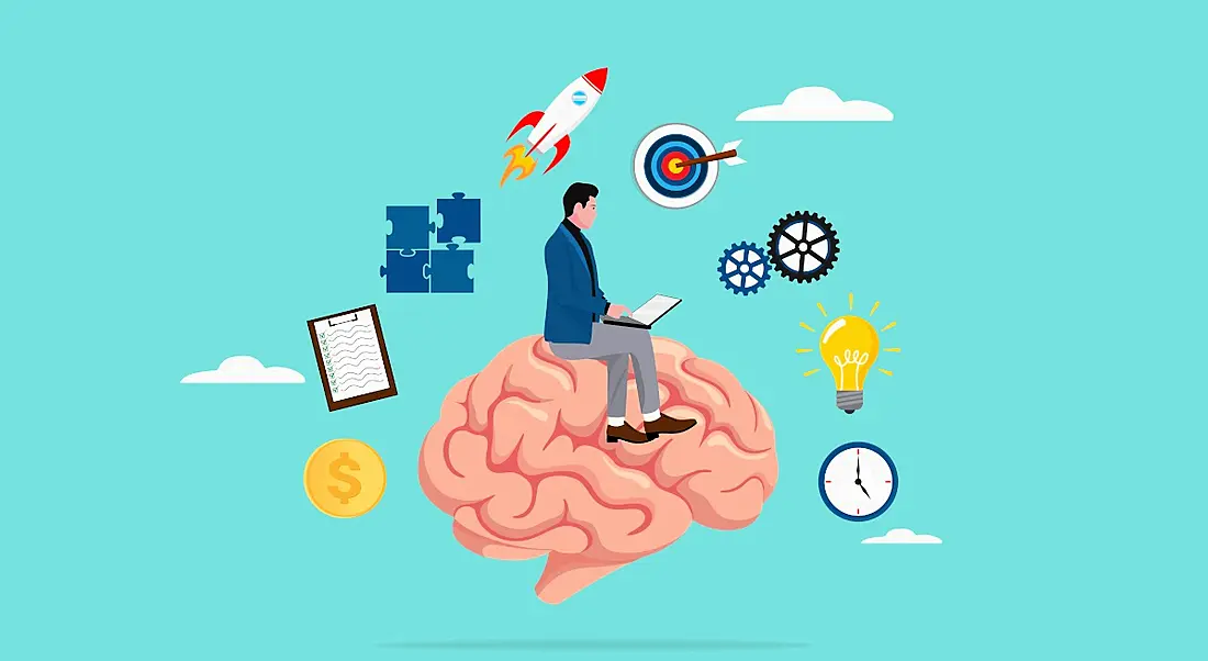 A cartoon image of a man working on a laptop while sitting on a brain. He is surrounded by symbols of learning, such as a jigsaw, a lightbulb and a bullseye.