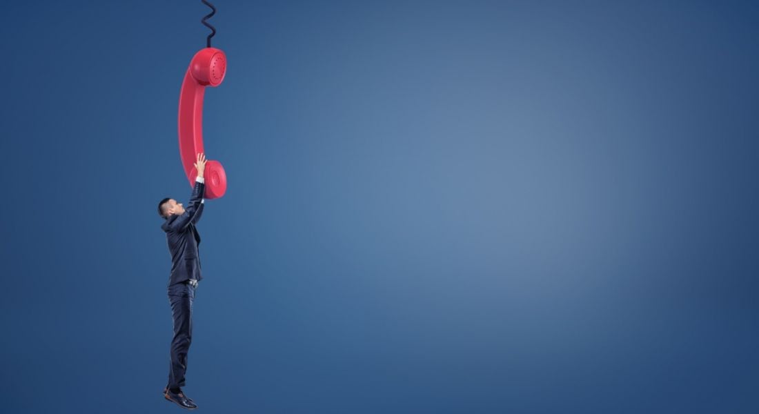 A man hangs on to a phone cord for dear life, representing the inability to disconnect from the workplace.