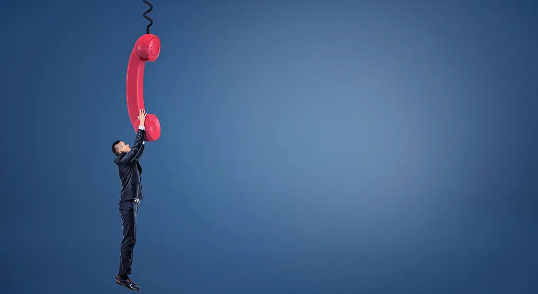 A man hangs on to a phone cord for dear life, representing the inability to disconnect from the workplace.