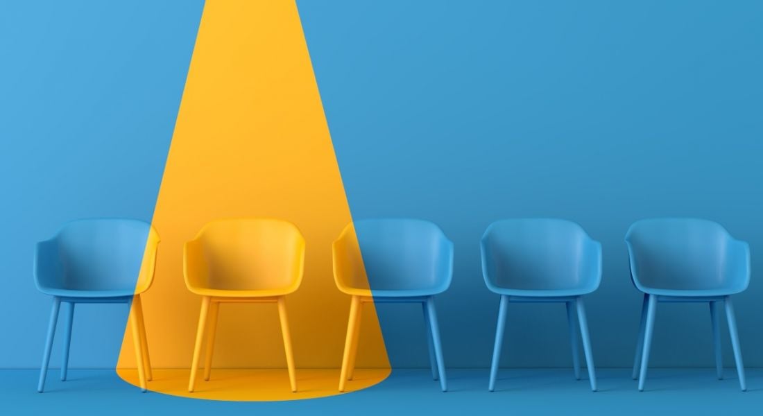 A yellow light shines on a blue room full of blue chairs, showing one person has been chosen for a job.