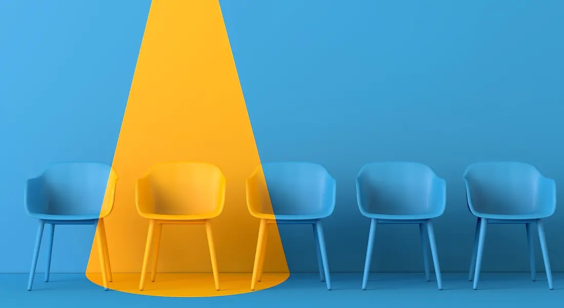 A yellow light shines on a blue room full of blue chairs, showing one person has been chosen for a job.