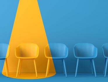 A yellow light shines on a blue room full of blue chairs, showing one person has been chosen for a job.