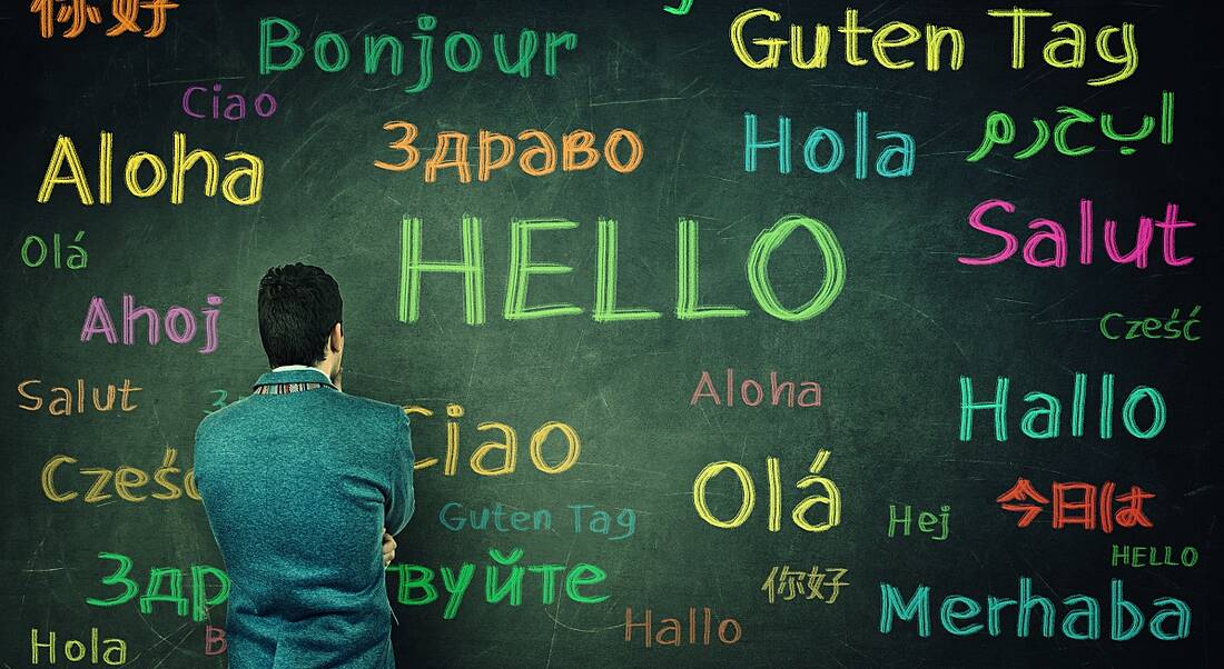 A man faces a board with the word hello spelt out in multiple different languages.