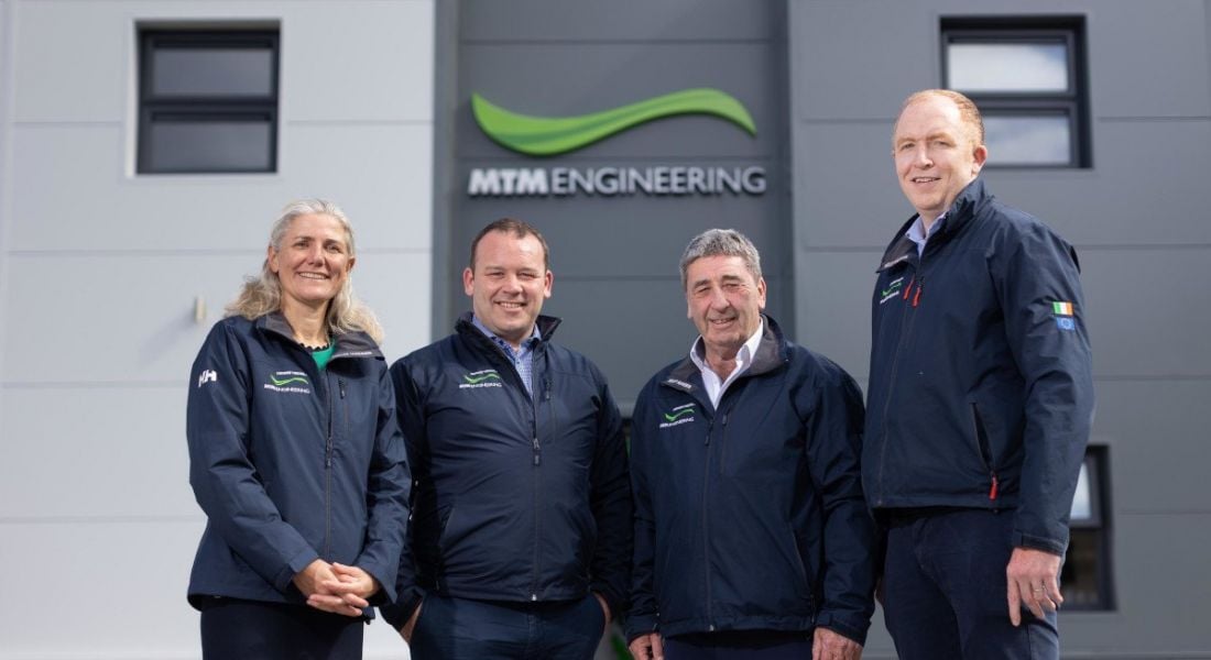 Three men and a woman standing in front of a building with the MTM Engineering logo on it.