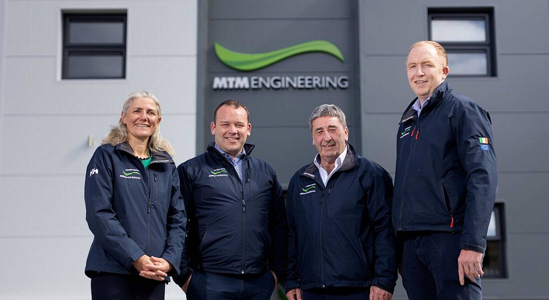 Three men and a woman standing in front of a building with the MTM Engineering logo on it.