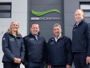 Three men and a woman standing in front of a building with the MTM Engineering logo on it.