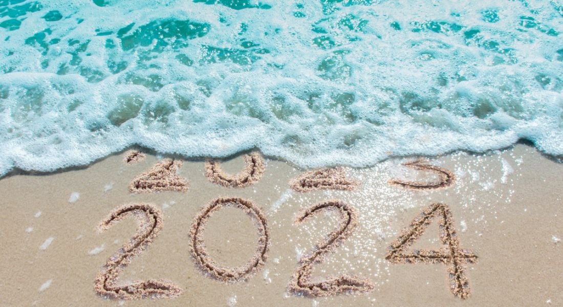 A wave on a beach washing over 2023 written in the sand so that only the numbers 2024 are visible written in the sand.