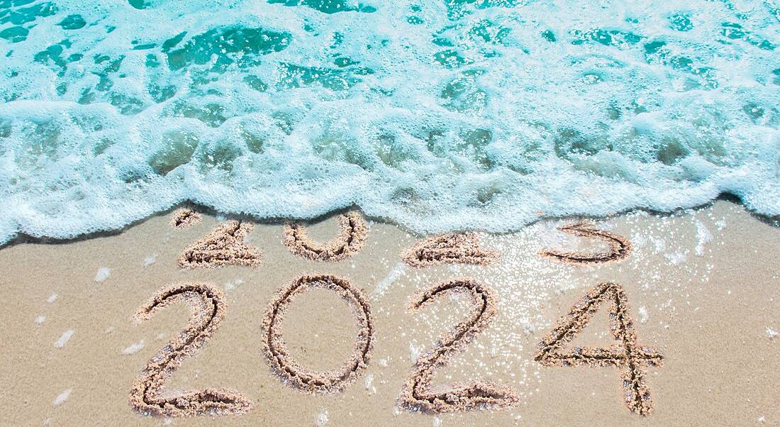 A wave on a beach washing over 2023 written in the sand so that only the numbers 2024 are visible written in the sand.