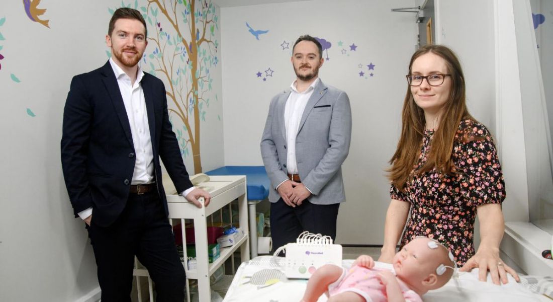 The three NeuroBell co-founders in a nursery with a baby doll in a child's cot.
