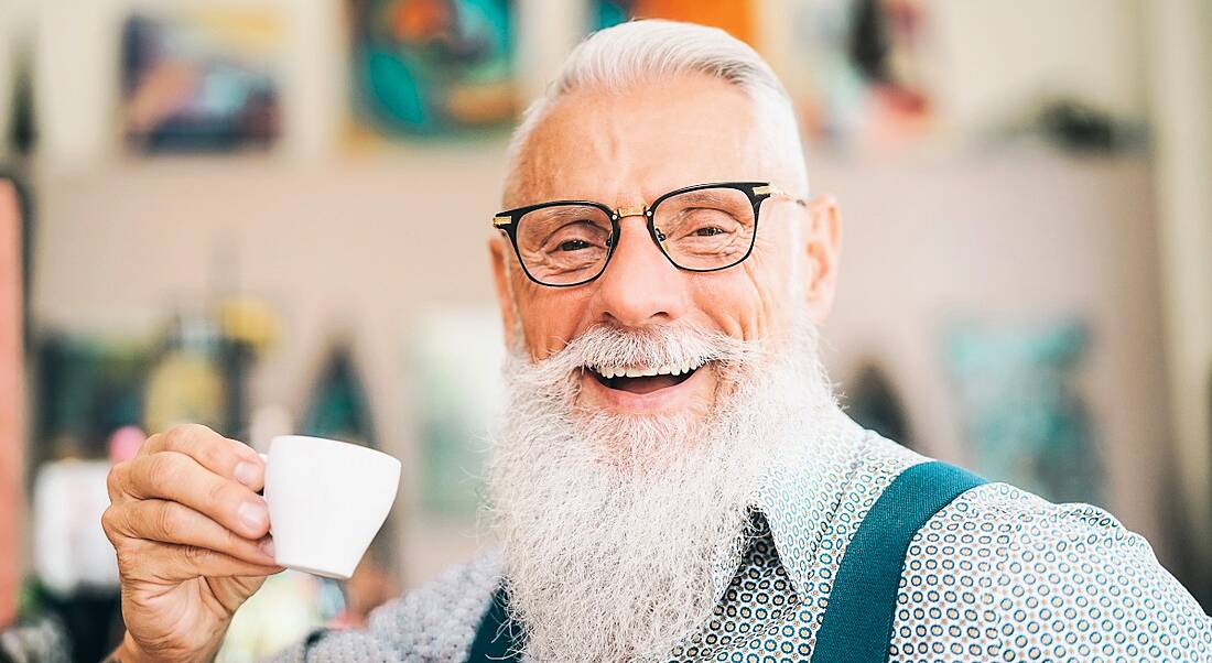 Older influencer and member of the creator economy sitting in a cafe drinking coffee.