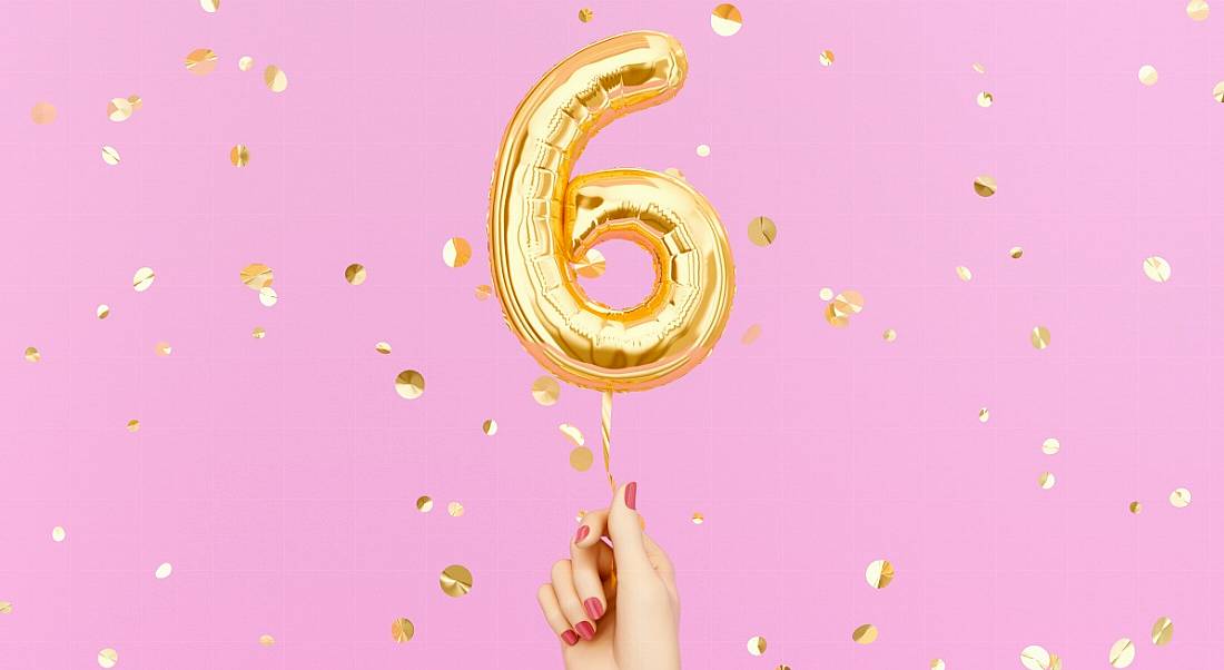 A hand with pink painted nails holding a gold balloon in the shape of a six on a pink background with sparkles.