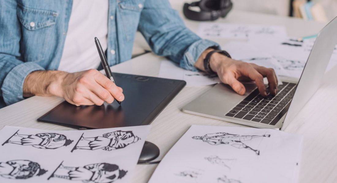 Animator working on a screen doing hand-drawn cartoons. He is also using a laptop.