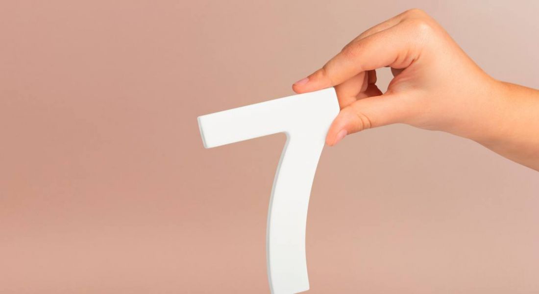 A person's hand visible holding a white number seven on a muted background.